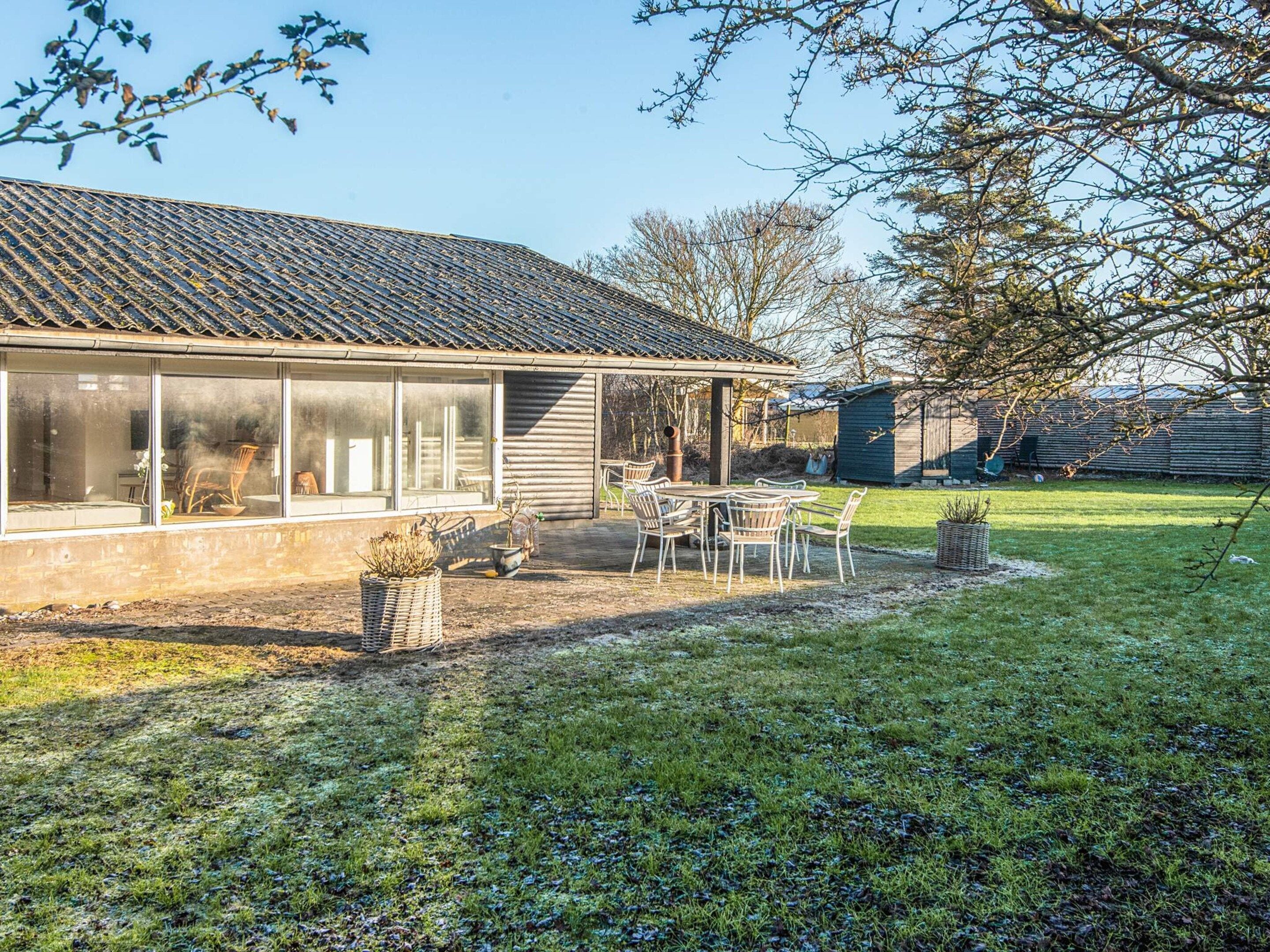 A house with a covered patio, a dining area with chairs, and a large window overlooking the yard.