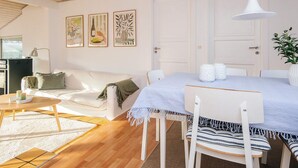 A modern living room with a white sofa, a dining table with chairs, a hanging light fixture, and framed artwork on the wall. - 6 Person Holiday Home in Juelsminde (Juelsminde)