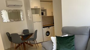 Een moderne woonkamer met een grijze bank, een eettafel met stoelen, een wasmachine en een magnetron op de achtergrond.
