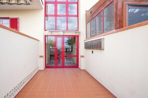 Ein Gang mit einer roten Tür, die zu einer Glastür führt, mit Fliesenboden und einem kleinen Fenster rechts.