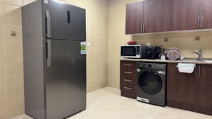 A compact kitchen with a stainless steel refrigerator, a microwave, a dishwasher, and wooden cabinets. - Spacious 2BR Apartment ,3 Bathrooms ,Near Mall (Abu Dhabi)