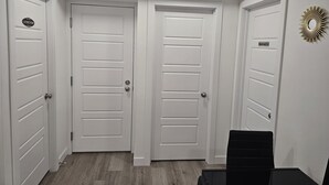 A hallway with three white doors, each marked with a sign indicating a laundry room and a restroom. - Cozy 1-bedroom Basement Suite With Private Entrance in Saskatoon (Saskatoon)