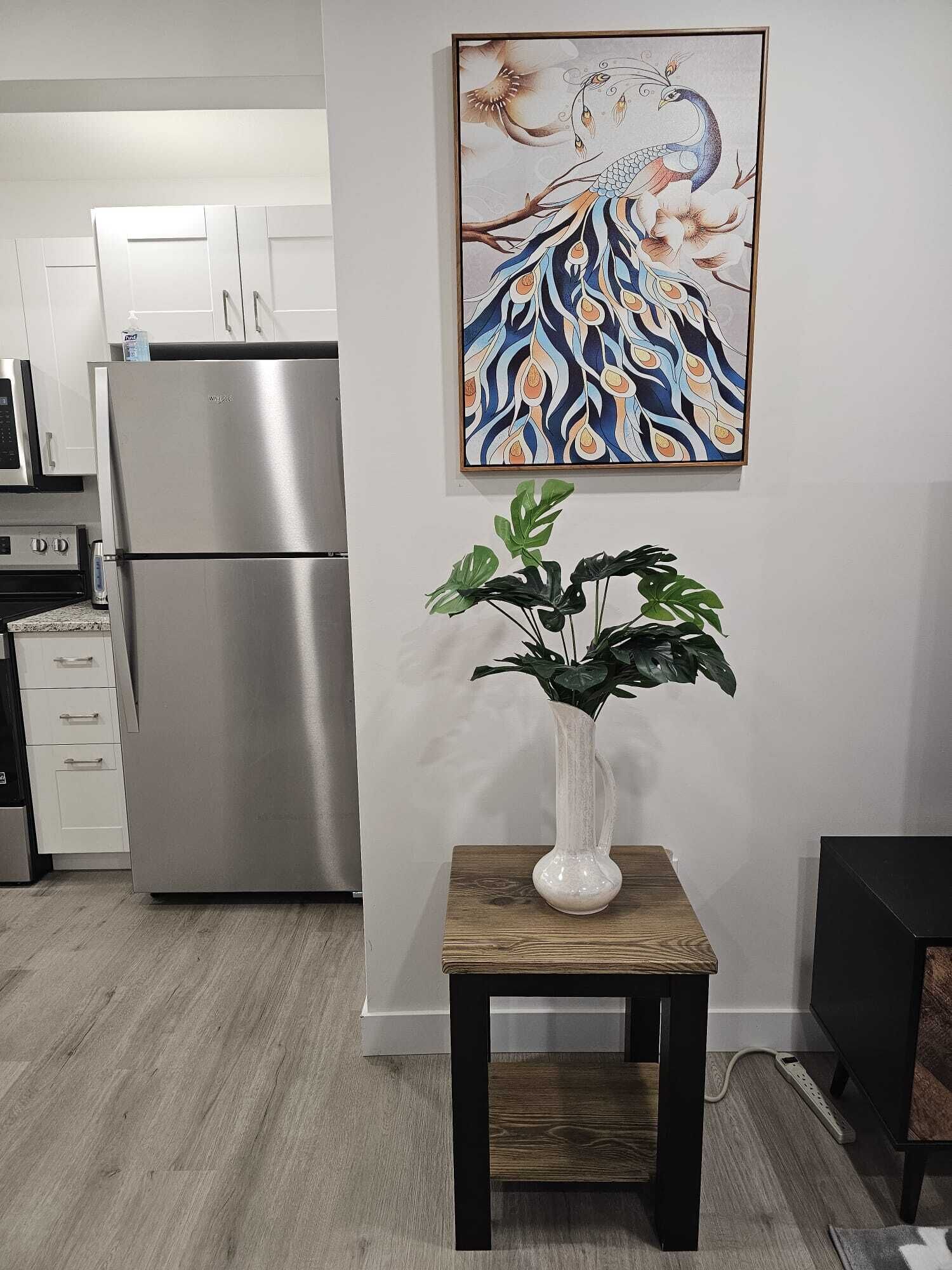 A kitchen with a stainless steel refrigerator, a white cabinet, and a wooden table with a vase of green plants.