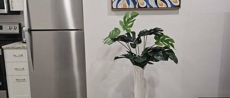 A kitchen with a stainless steel refrigerator, a white cabinet, and a wooden table with a vase of green plants.