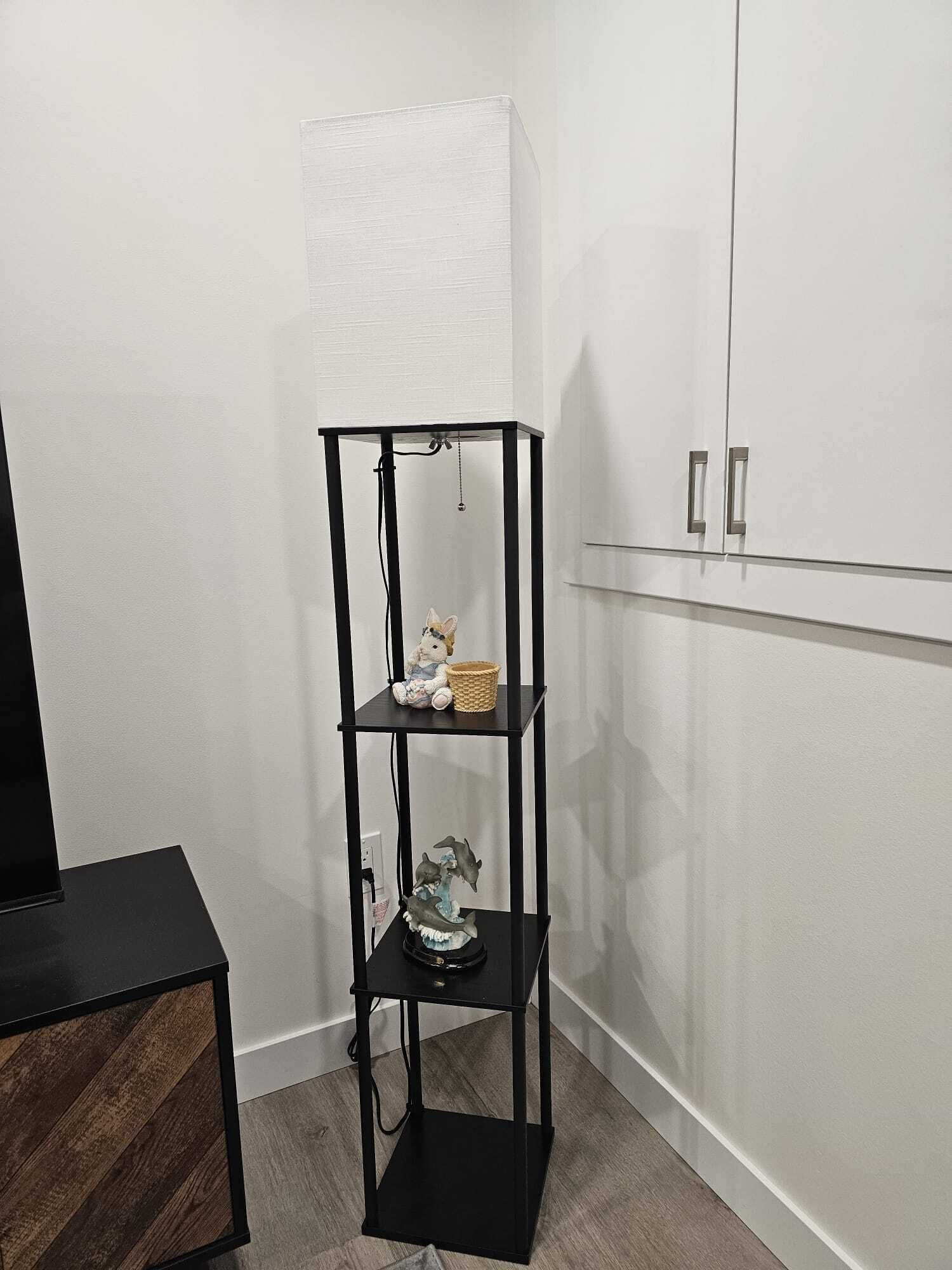 Une étagère en métal noir, composée de trois étagères, avec un petit panier et un objet décoratif placé sur l’étagère supérieure.