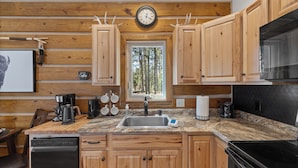 A kitchen with wooden cabinets, a granite countertop, a sink, a stove, and a clock on the wall.