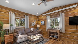 A cozy cabin interior with a wooden interior, a sofa, a coffee table, and a TV mounted on the wall.