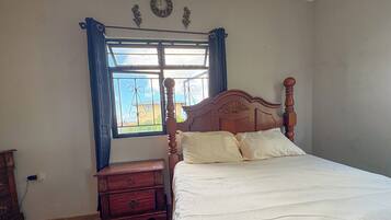 Une chambre à coucher avec un lit en bois, une table de chevet, une commode et une fenêtre avec des rideaux.