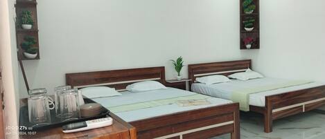 A hotel room with two wooden beds, a bedside table with a lamp, a small potted plant, and a shelf with decorative items.