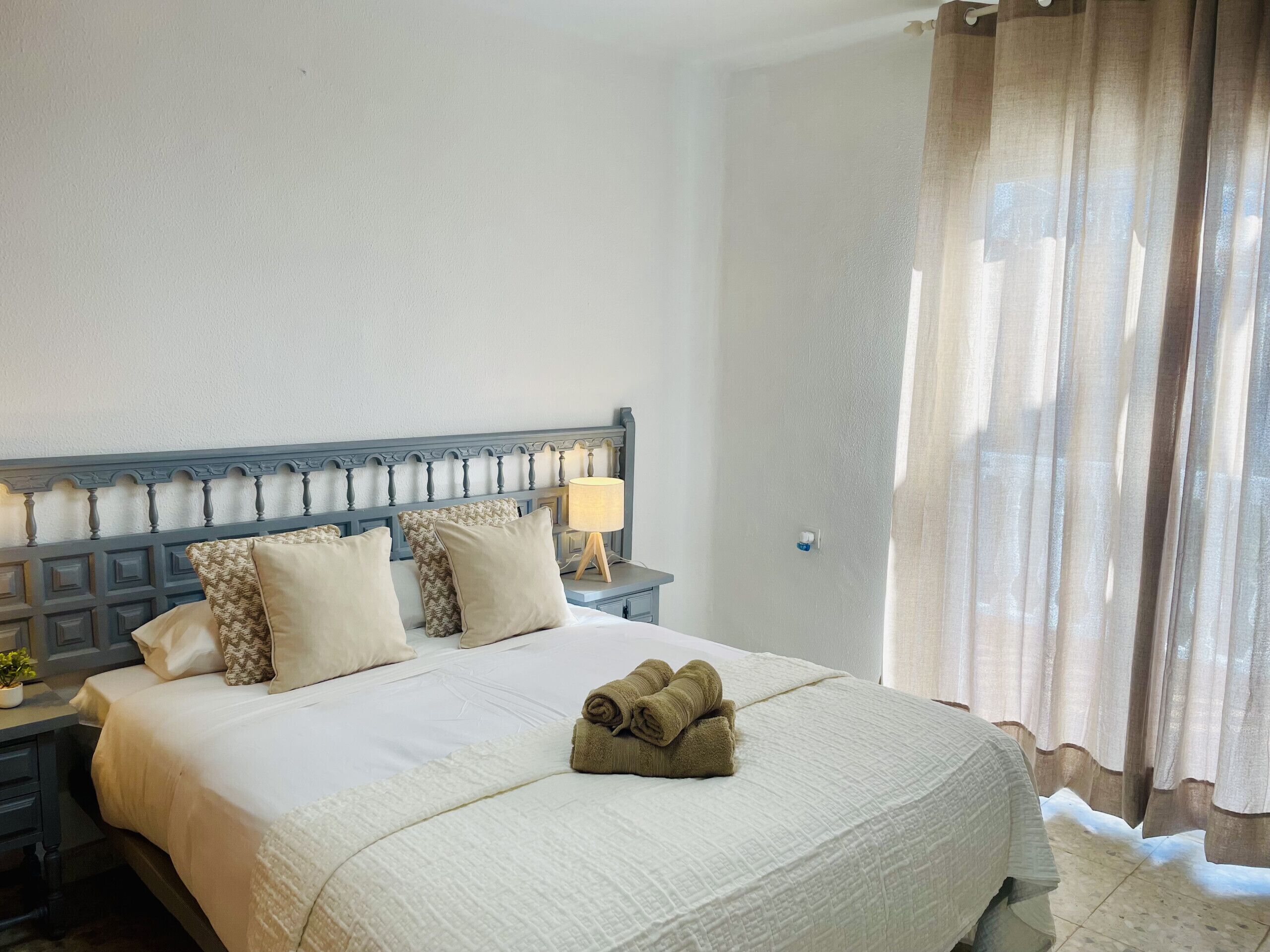Una cama bien hecha con cabecera, almohadas y una toalla enrollada.