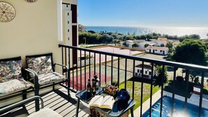 A balcony with a view of the sea, a pool, and a table with books and bottles. - Mirador del Faro Apartment Torrox Costa (Torrox Costa)