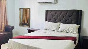 Slaapkamer met een groot bed, hoofdeinde, airconditioning, spiegel en raam met gordijnen.