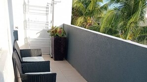 Een balkon met rieten meubels en een glazen tafel, met uitzicht op een palmboom.