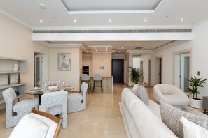 Un vaste espace de vie doté d’un plafond haut, d’une table à manger pour quatre personnes et d’un coin salon avec des canapés et des fauteuils.