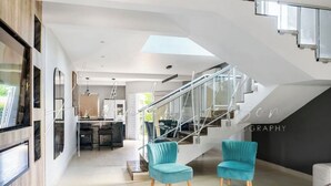 Um interior moderno com escada, duas cadeiras verde-turquesa e uma área de jantar.