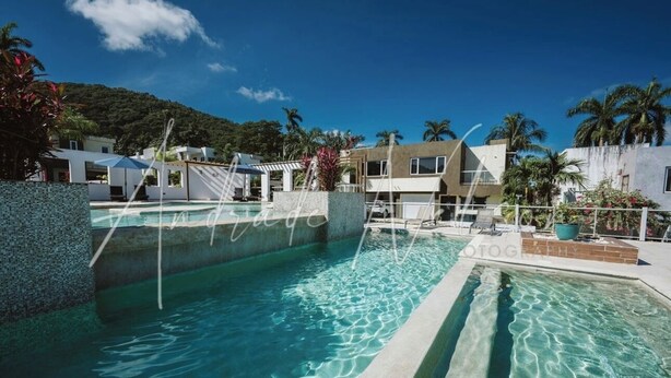 Uma piscina com água cristalina, rodeada por edifícios modernos e palmeiras.