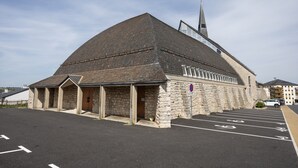 A church with a stone facade, a steeple, and a parking lot with marked spaces. - Le Cyclactus (ex-Cyclamens) - Rodez-Onet (Onet le Château)