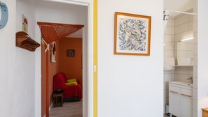 A hallway with a red chair, a wooden bench, a hammock, and a framed artwork on the wall. - Le Cyclactus (ex-Cyclamens) - Rodez-Onet (Onet le Château)