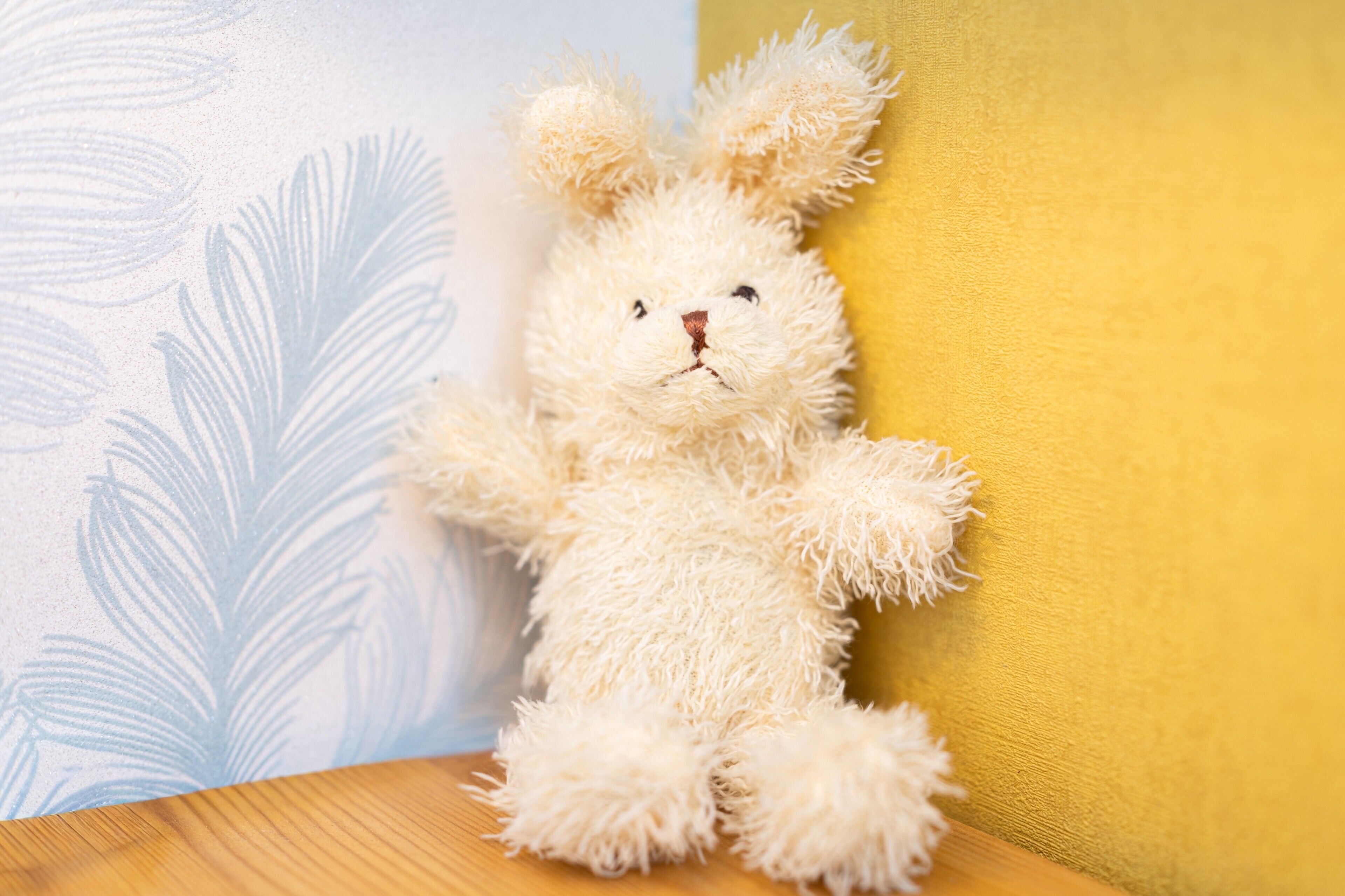 Ein Kuscheltier vor einer Wand mit Blattmuster und einfarbiger Gestaltung.
