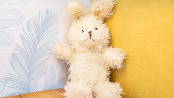 Un jouet en peluche appuyé contre un mur orné d’un motif de feuilles et d’une couleur unie.