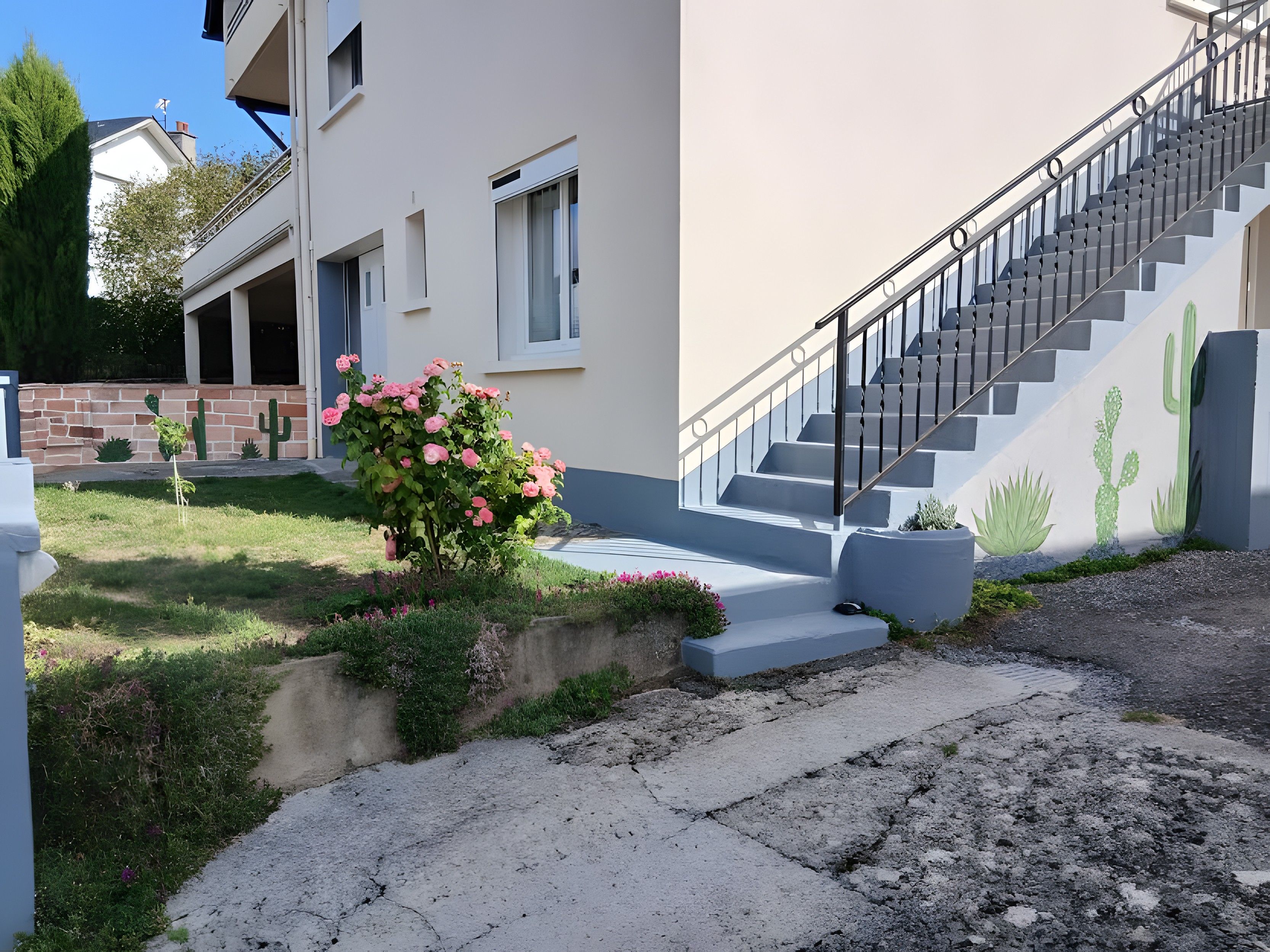 A residential building with a staircase, a small garden with pink flowers, and a cactus mural on the wall.