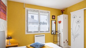 A bedroom with a bed, a bedside table with a lamp, a radiator, a wardrobe, and a window with a view of the outside. - Le Cyclactus (ex-Cyclamens) - Rodez-Onet (Onet le Château)