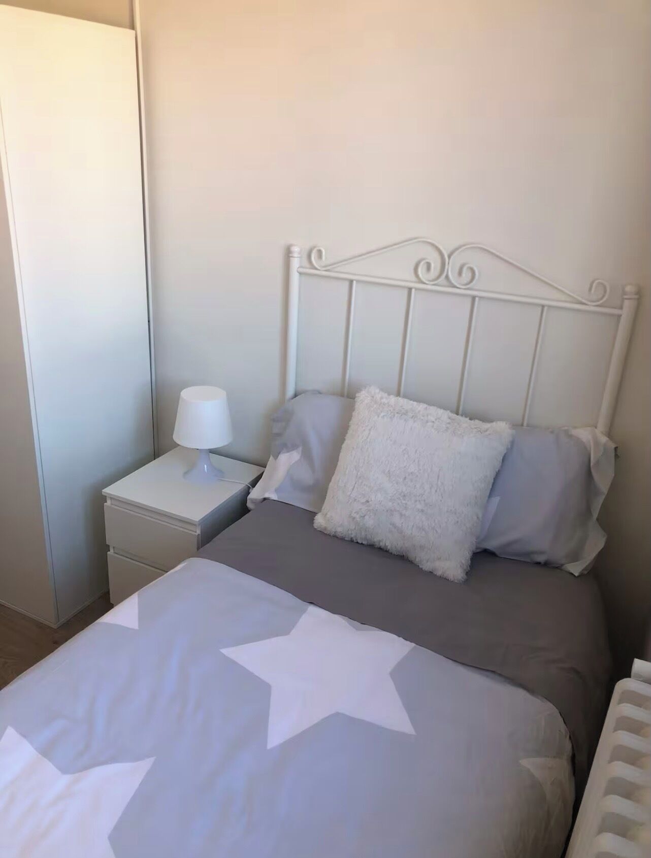 Una cama bien hecha con una colcha de estampado de estrellas, un cabecero de metal blanco y una mesita de noche con una lámpara.