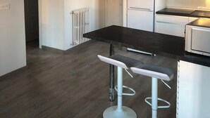 Une cuisine moderne avec des armoires blanches, un comptoir noir et des appareils en acier inoxydable. On y trouve deux tabourets de bar blancs et une suspension au-dessus du comptoir.