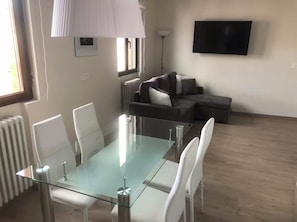A modern living room with a glass-top dining table, white chairs, a grey sofa, and a flat-screen TV mounted on the wall. - Apartment Catedral with wifi VUT-LE-573 (León)