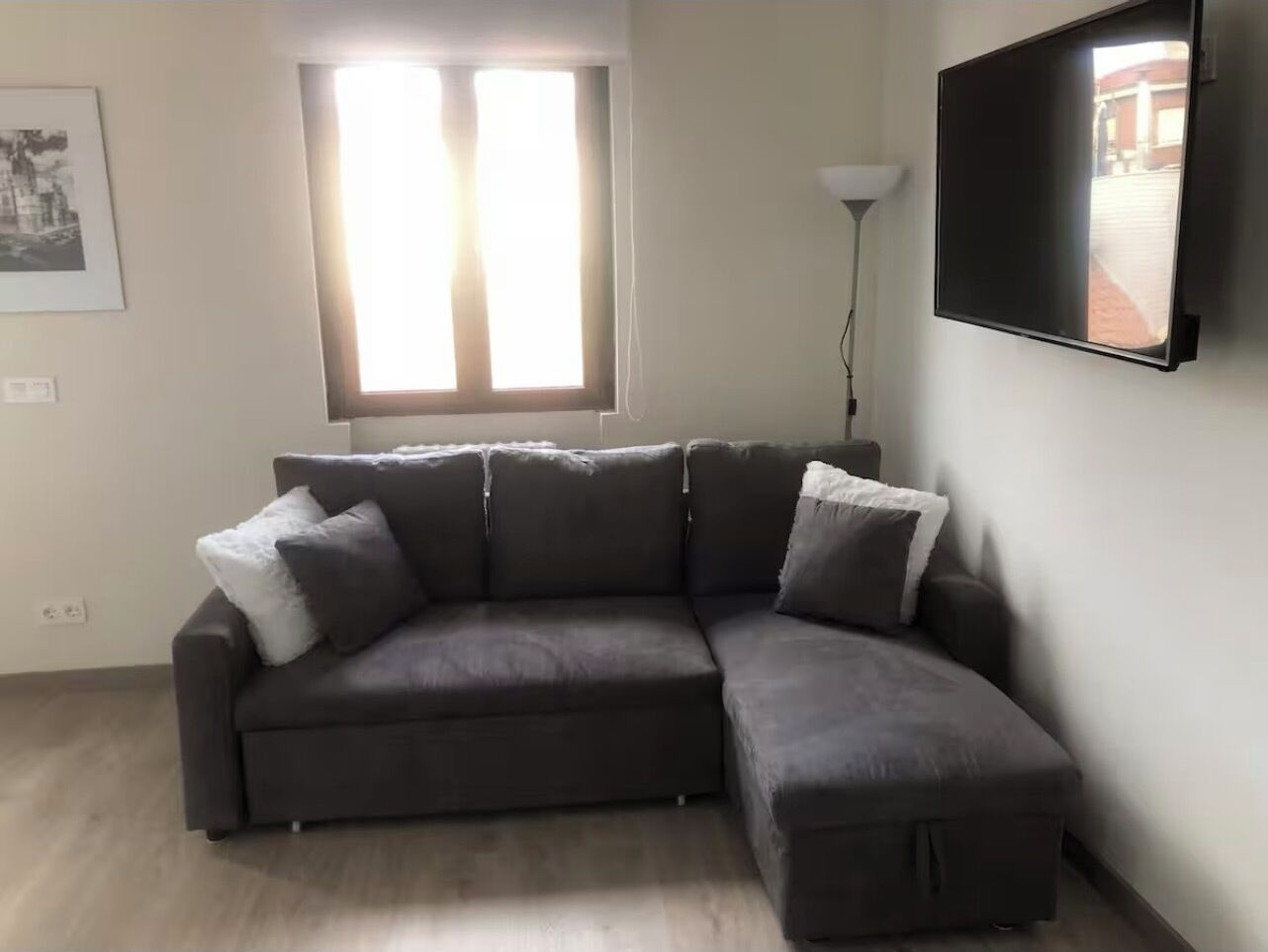 Ein modernes Wohnzimmer mit einem Ecksofa, einem flachbildfernseher an der Wand und einem Fenster mit Vorhängen.