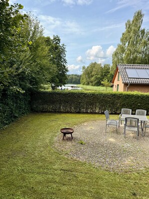 Een gazon met een tafel en stoelen, een vuurkorf, en een gebouw met een betegeld dak.