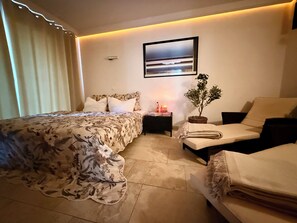A hotel room with a bed, a chair, a nightstand, a potted plant, and a wall-mounted picture. - Green cottage with sauna, 5 * by the lake (Lohmen)