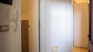 Habitación de hotel con piso de madera, una puerta blanca con el cartel 'SP4', un teléfono blanco fijado a la pared y un interruptor de luz.