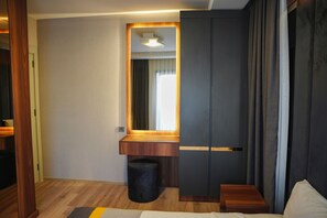 A modern hotel room with a wooden desk, a large mirror, a bed, and a wardrobe.