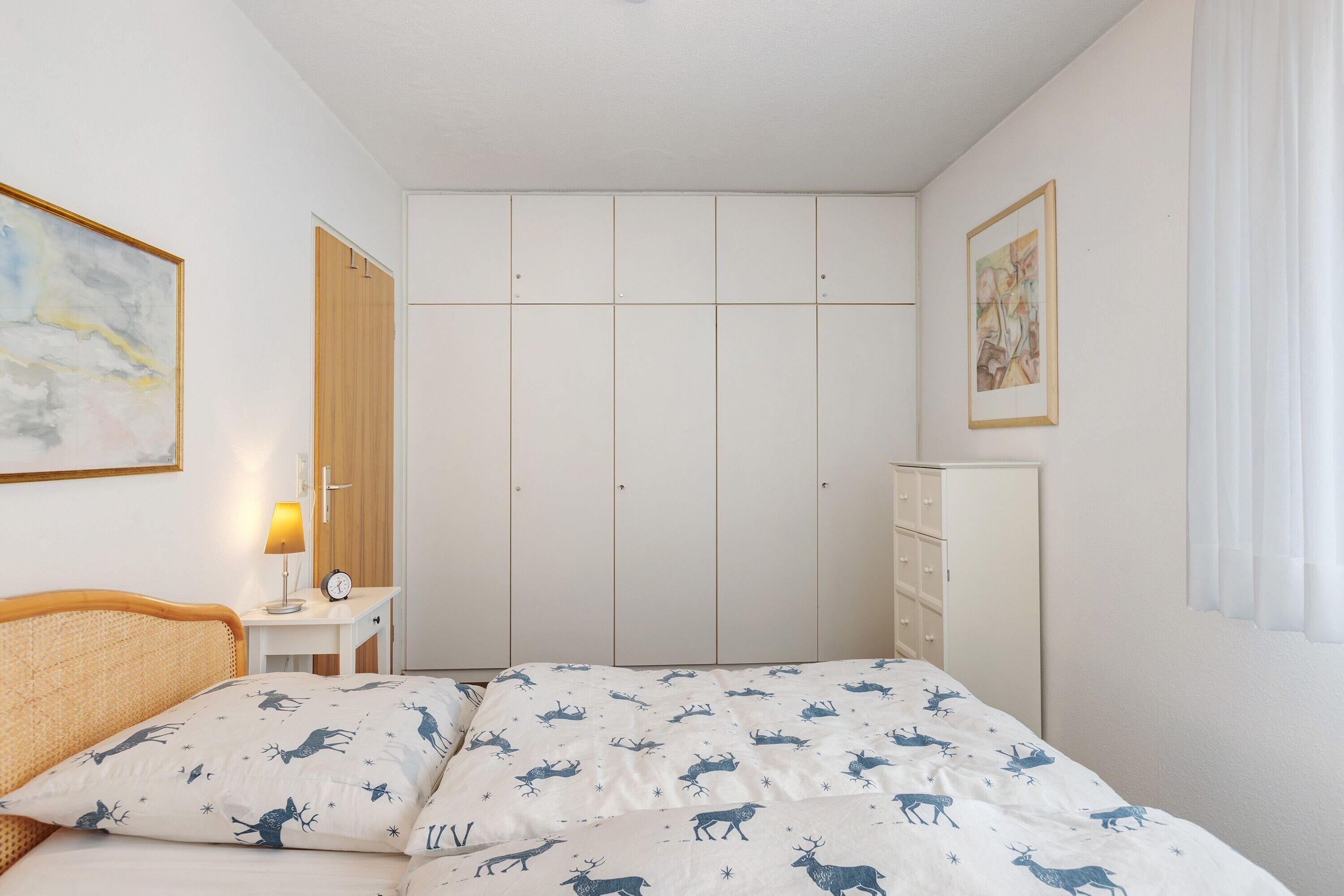 Een slaapkamer met een bed, nachtkastje, lamp, kledingkast en een schilderij aan de muur.