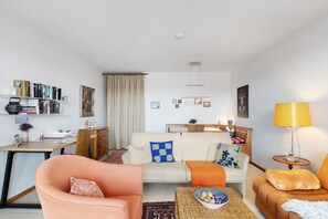 Una sala de estar con un sofá, sillones, una mesa de centro, una lámpara, una estantería y un cuadro en la pared.