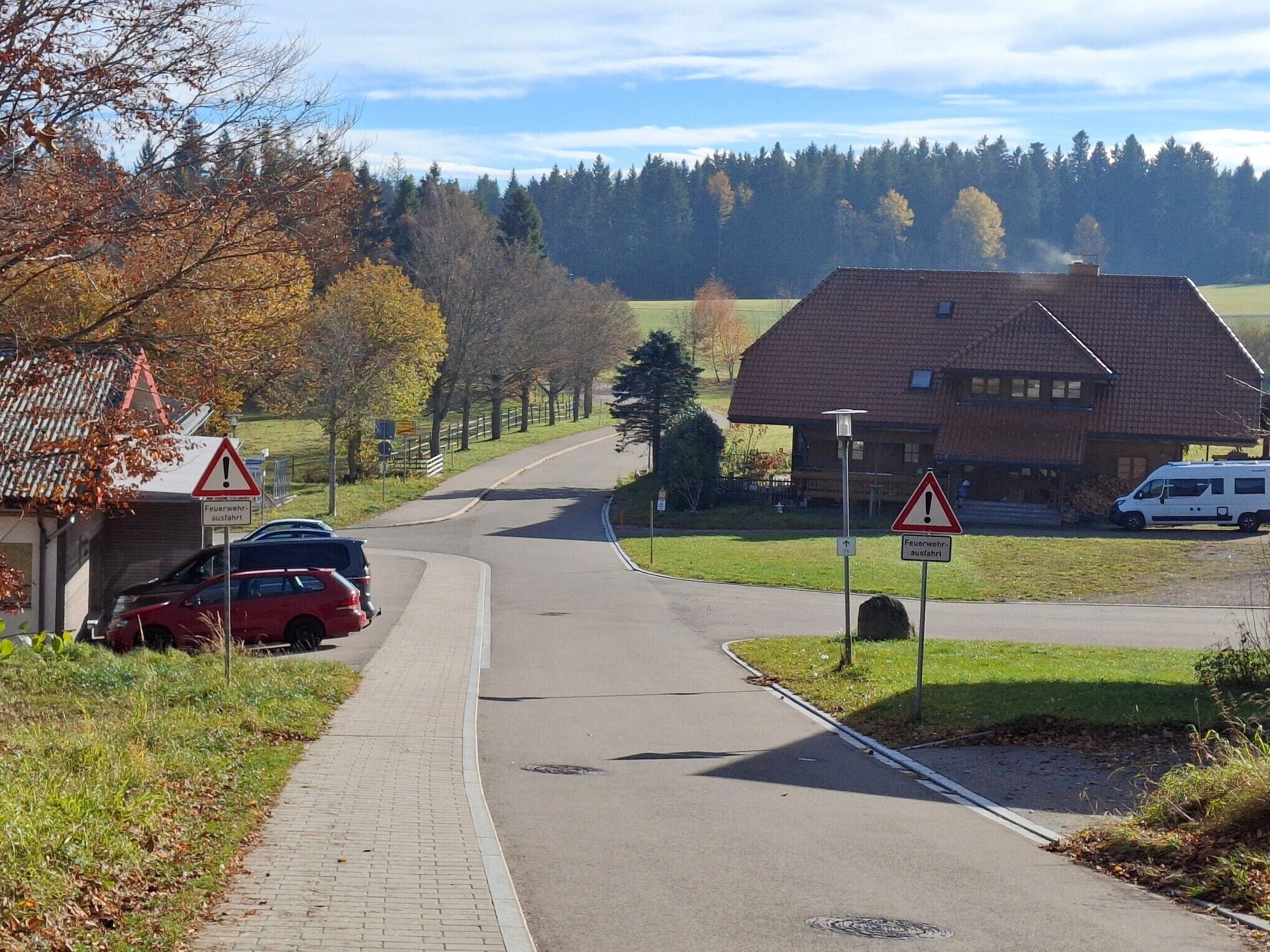 En landsväg med en kurva, en röd bil parkerad vid vägkanten och en byggnad med ett rött tak i bakgrunden.