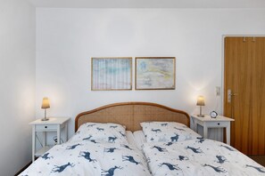Un dormitorio con una cama, dos mesitas de noche, una puerta de madera y dos cuadros colgados en la pared.