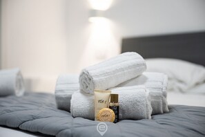 A neatly made bed with folded white towels, a tube of Ivory soap, and a bottle of VOR® body wash.