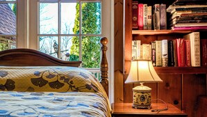 A bedroom with a bed, a bedside table with a lamp, and a bookshelf filled with books. - Highland Ave (Norwalk)