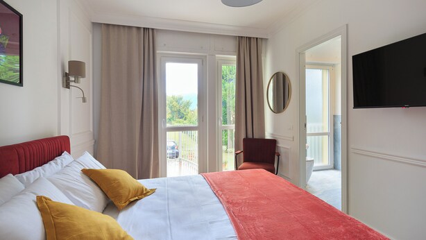 Habitación de hotel con cama, televisión, una silla y balcón con vistas.