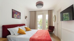 Una habitación de hotel con cama, una silla, televisión y ventana con cortinas.