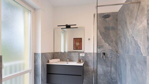 Un baño moderno con cabina de ducha de vidrio, un lavabo empotrado con tocador oscuro y un espejo grande encima del tocador.