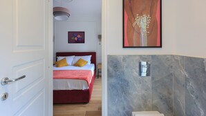 Habitación de hotel con cama, puerta, baño con ducha y un cuadro en la pared.