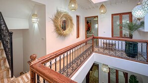 A multi-level interior with a staircase, decorative wall hangings, and hanging lights. - Riad Louzaia Marrakech (Marrakech)