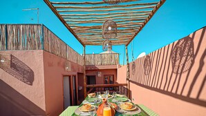 An outdoor dining area with a table set for a meal, surrounded by a wooden pergola and a tiled floor. - Riad Louzaia Marrakech (Marrakech)