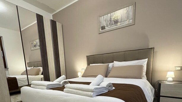 Un dormitorio de hotel moderno con una cama grande, una mesita de noche con lámpara, un espejo y un cuadro en la pared.