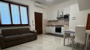Una cocina moderna con armarios blancos, un microondas y una estufa a gas. Hay una mesa de comedor con sillas y un sofá en la sala de estar.