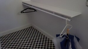Ein kleiner, schmaler Raum mit einem Schachbrettboden, einer weißen Wand und einem weißen Regal mit schwarzen Kleiderbügeln.