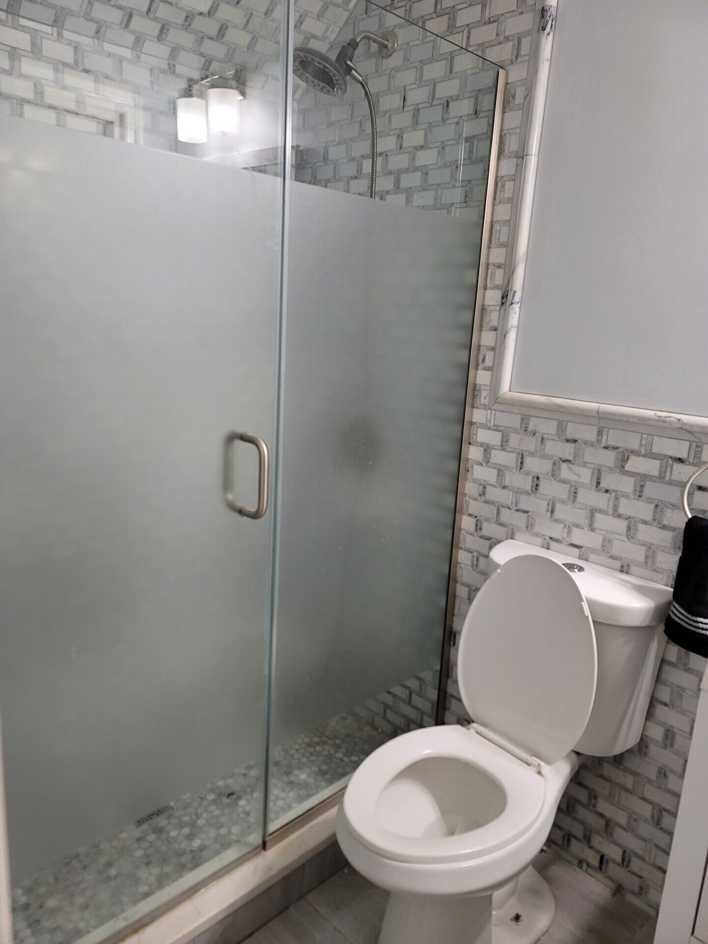 Een badkamer met een douche met glazen wand, een wit toilet en een betegelde muur.